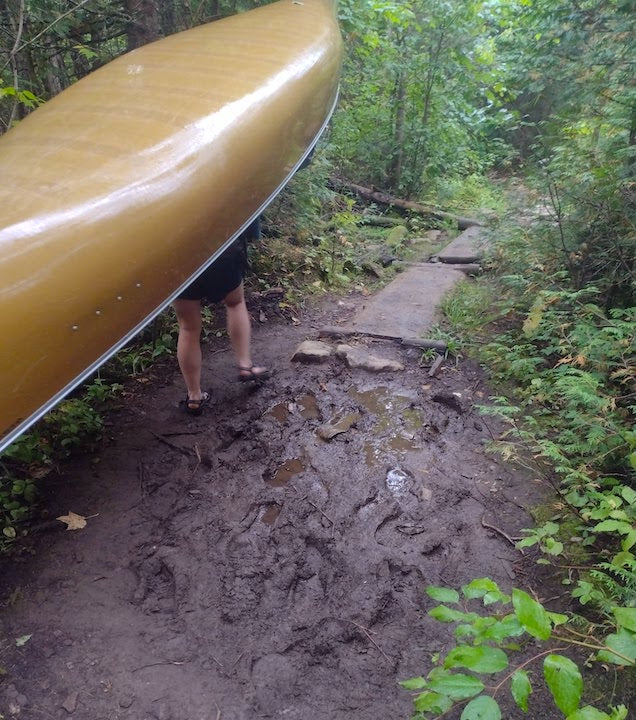 woman portaging a canoe on a muddy trail