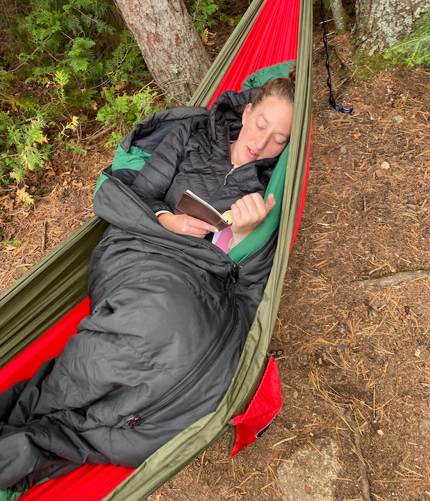 woman laying in hammock at camp, reading