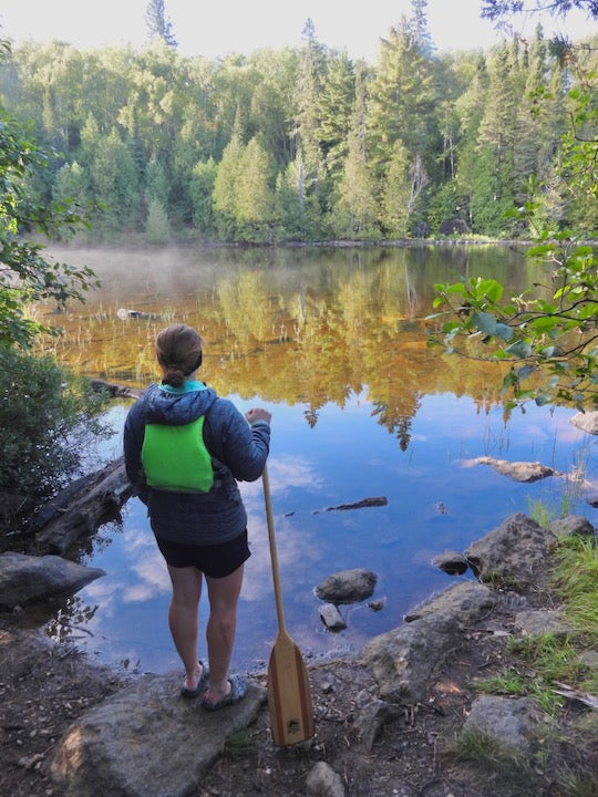 woman standing with her paddle overlooking a calm bay