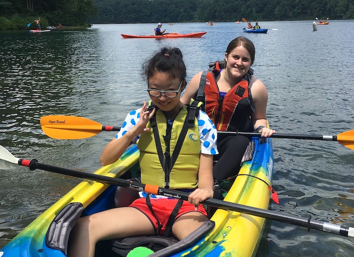 two women in a kayak on the water with other kayakers in the background