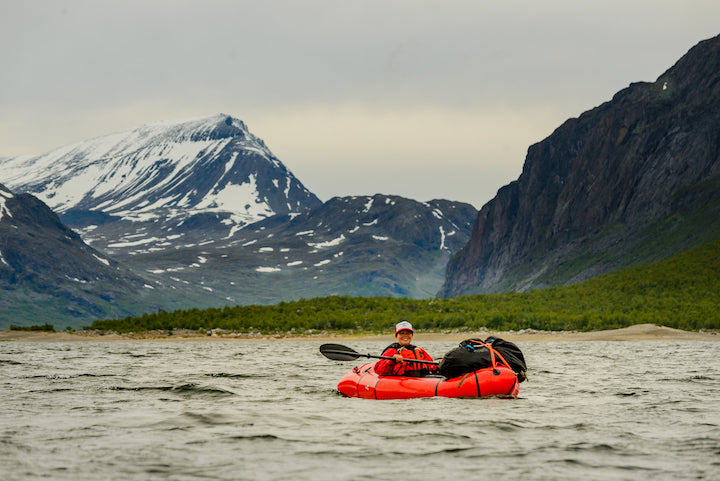 Katja Koskinen packrafting on a lake with mountains in the background