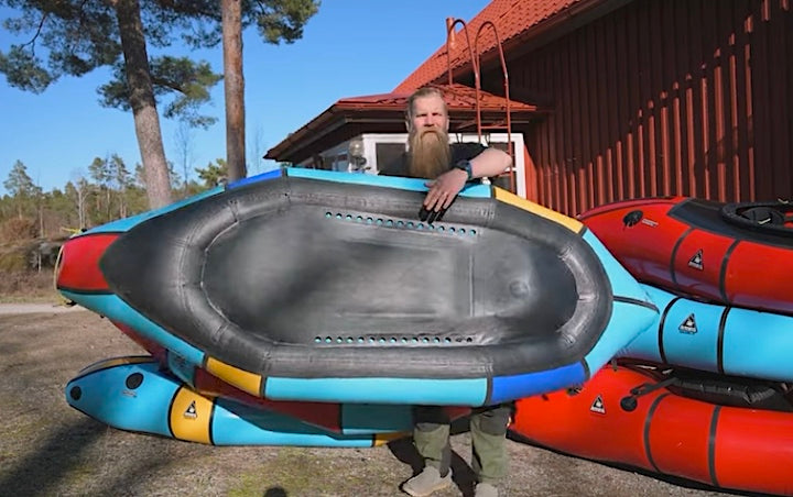 Caj holds up his packraft to show the self-bailing holes on the hull