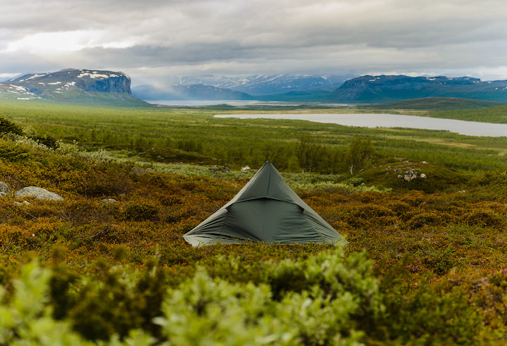 small tent on the ground, river and mountains in the background