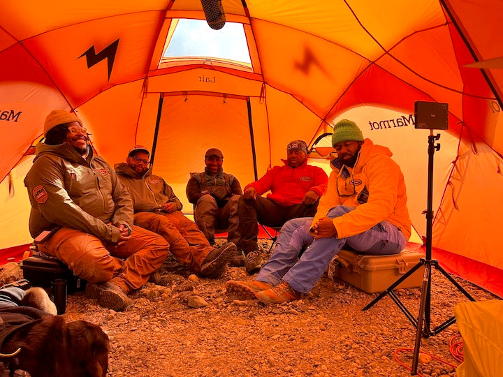 five men sit inside a tent while filming