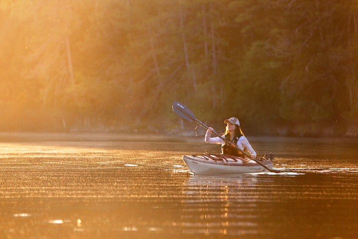 woman kayaking on a lake at sunset