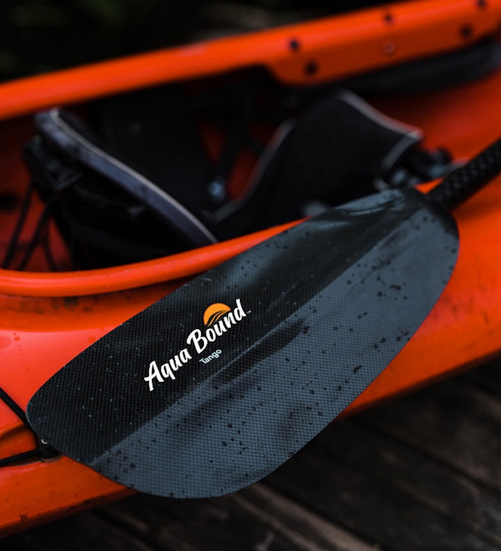 blade of an Aqua Bound carbon kayak paddle sitting on a red kayak