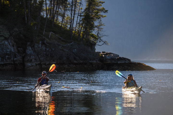 man and woman kayaking in low light, rocky island in the background