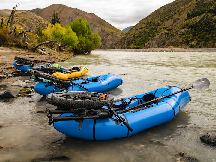 four packrafts lined up along the river, loaded with bikes and paddles