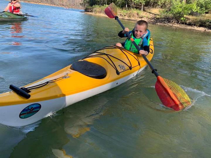 little boy paddles an adult size sit-in kayak