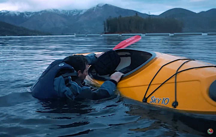 man about to climb back in a capsized kayak