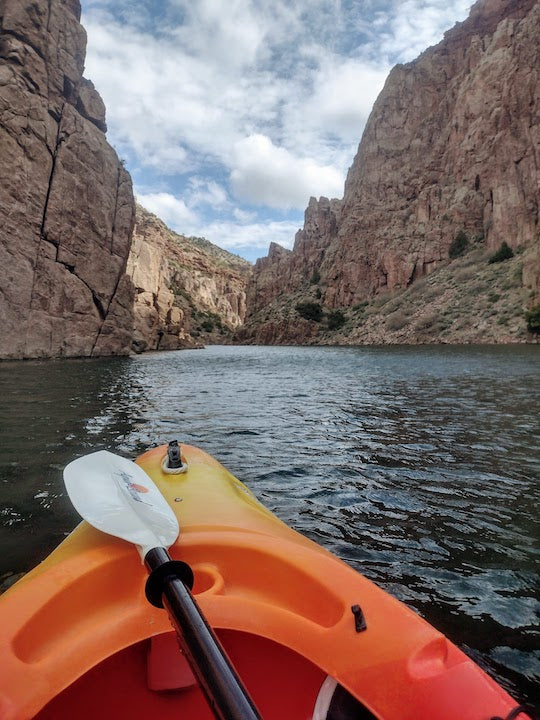 orange kayak with Aqua Bound paddle on the water inside Fremont Canyon; canyon walls high on either side