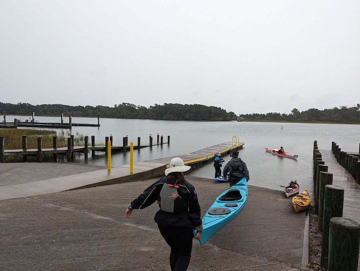 people carry a kayak to the water, others already on the water paddling