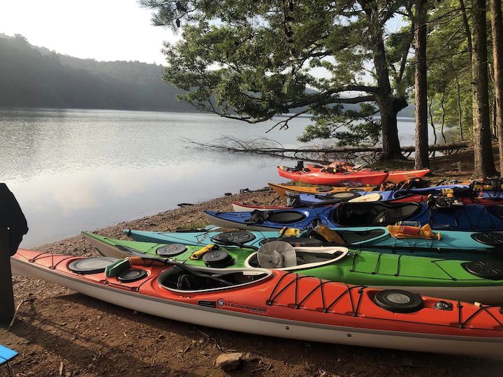 row of kayaks on shore next to a river, ready to a day of touring