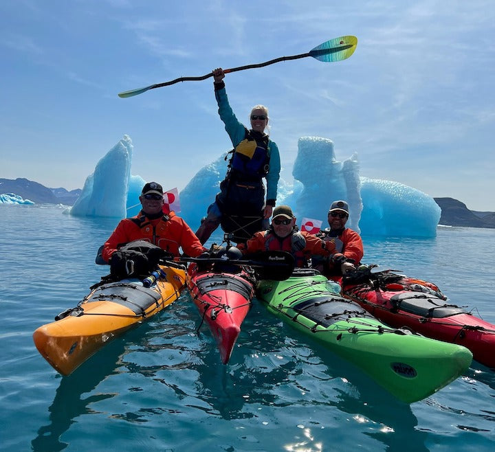 4 sea kayakers in front of ice bergs, one standing on her kayak