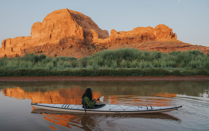 man in white kayak on a river in front of canyon formations