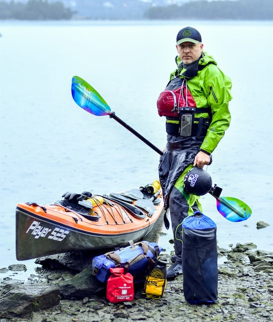 man standing next to his kayak with all kinds of gear