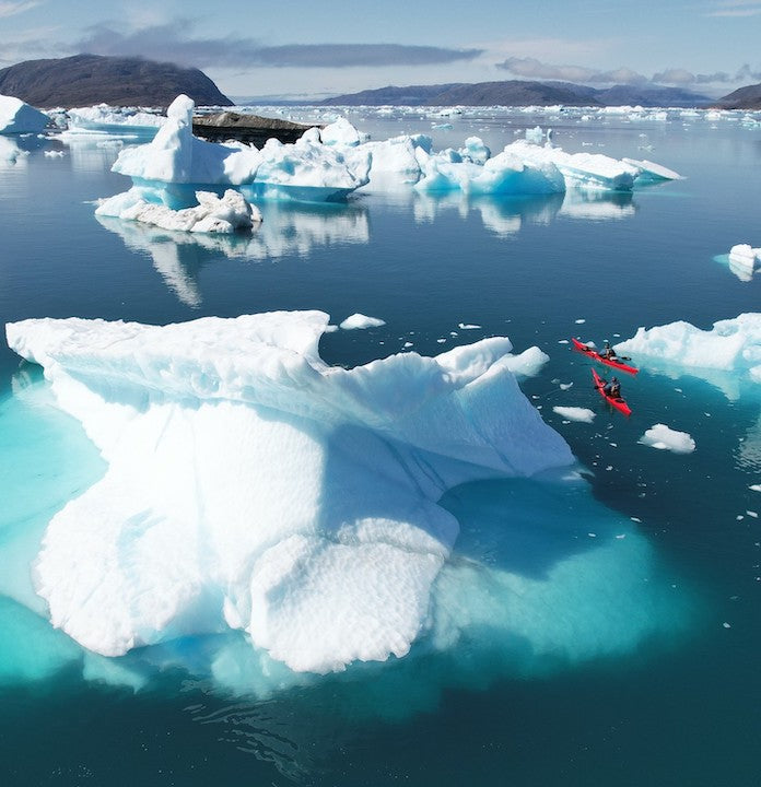 drone shot of two sea kayakers paddling among Greenland's icebergs