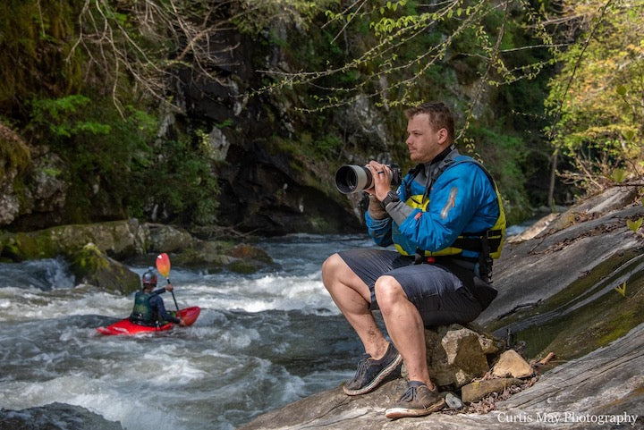 Jonny Ortiz sits next to a whitewater river with his camera