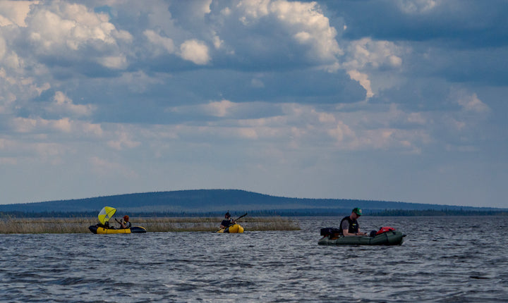 three packrafters on a large lake under storm clouds