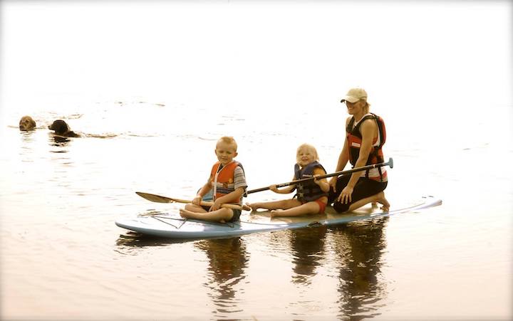 woman paddle boarding with two young children