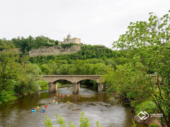 LWA packrafting group on a river in Germany, under a stone bridge with a castle in the upper background