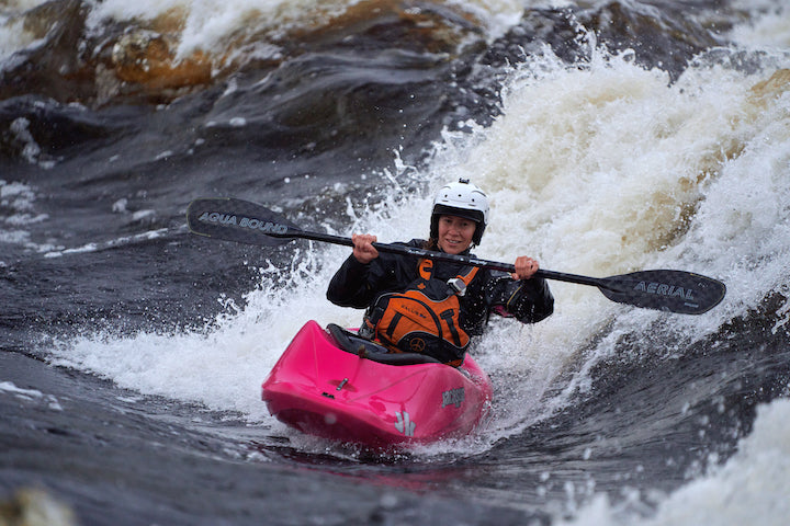 woman whitewater kayaker coming off a wave, uses Aerial paddle