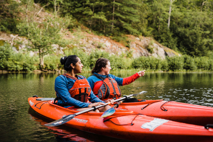 two women in red kayaks along a rocky shoreline