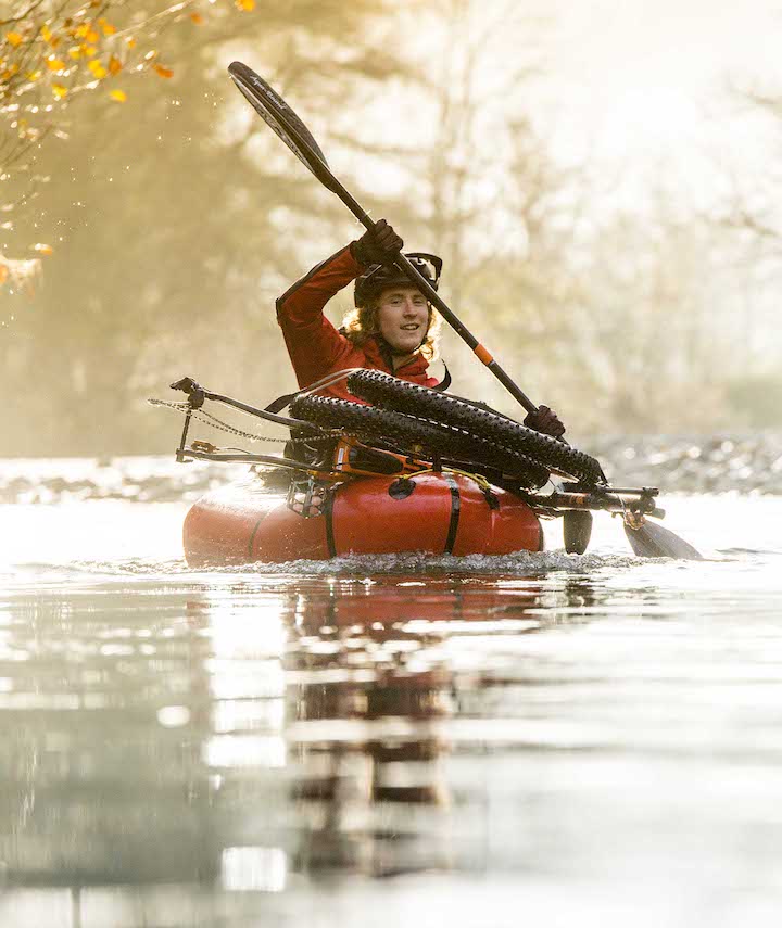 man paddling a packraft with a bike strapped to the top