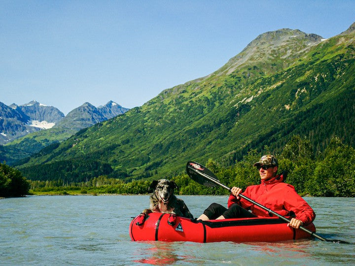 a man packrafts with his dog on a mountainous lake