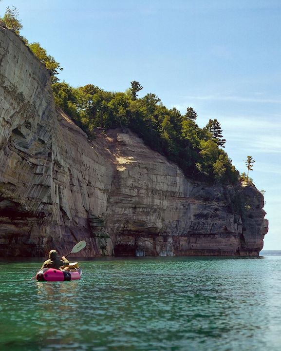 packrafter paddling alongside high cliffs
