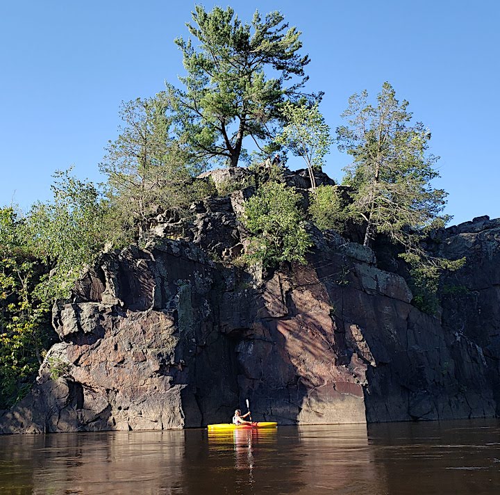 kayaker in a yellow kayak makes a great focal point in front of a rocky shoreline's deep shadows