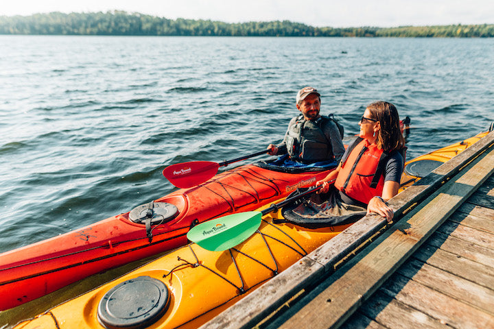 a man and woman in two kayaks at the dock, ready to get on the water