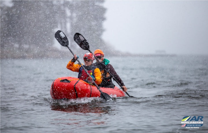 two paddlers in a tandem packraft on a lake in the snow