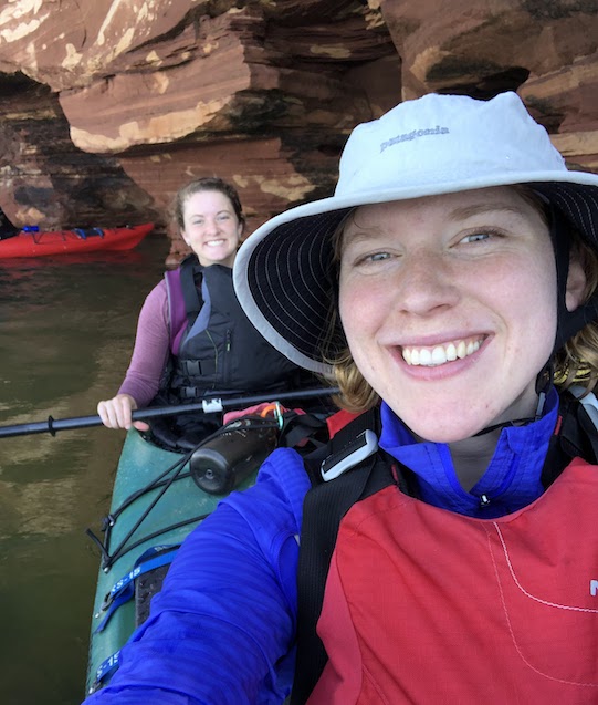 Rachel in front with her kayak mate behind her, on the water in front of sea caves