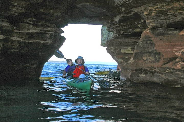 two women in a tandem kayak paddle through a sea cave