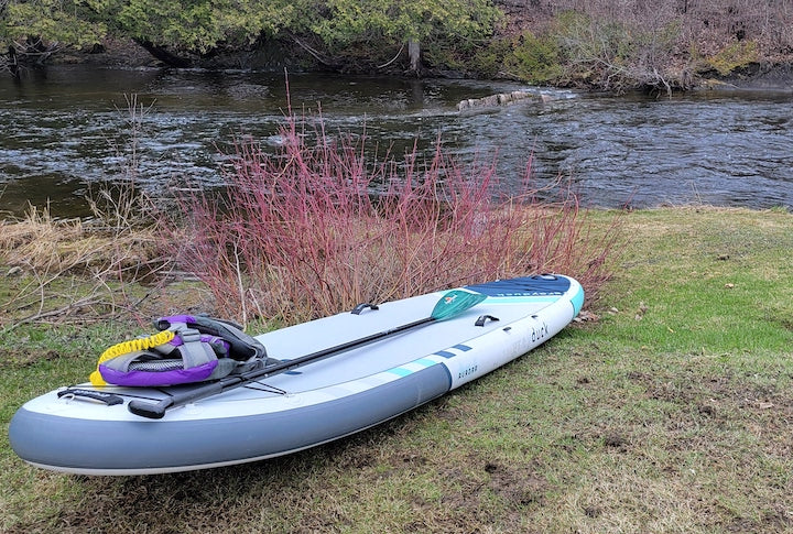 inflatable paddleboard with pdf and paddle next to a river