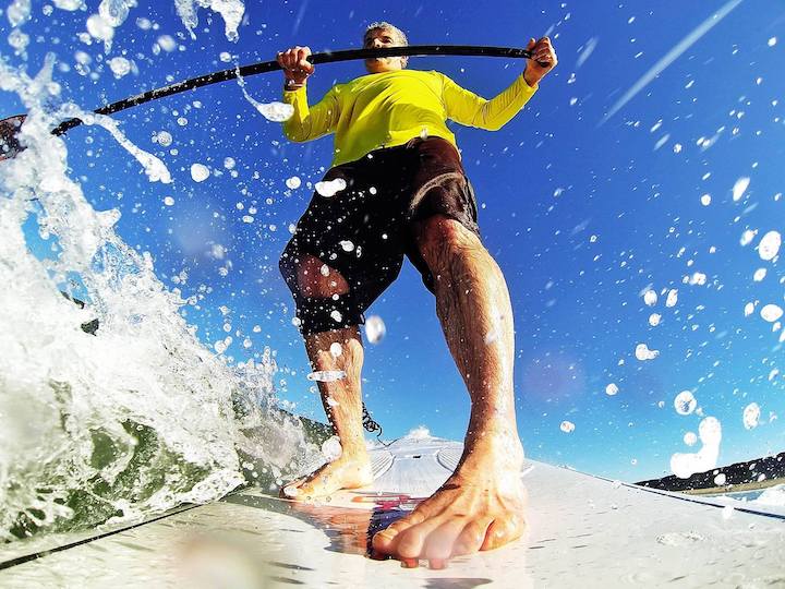 close up of a man paddleboarding in waves, wearing SUP leash