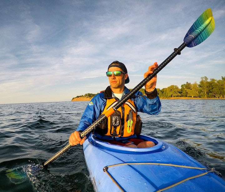 man kayaking on a large lake wearing sunglasses, shoreline in the background