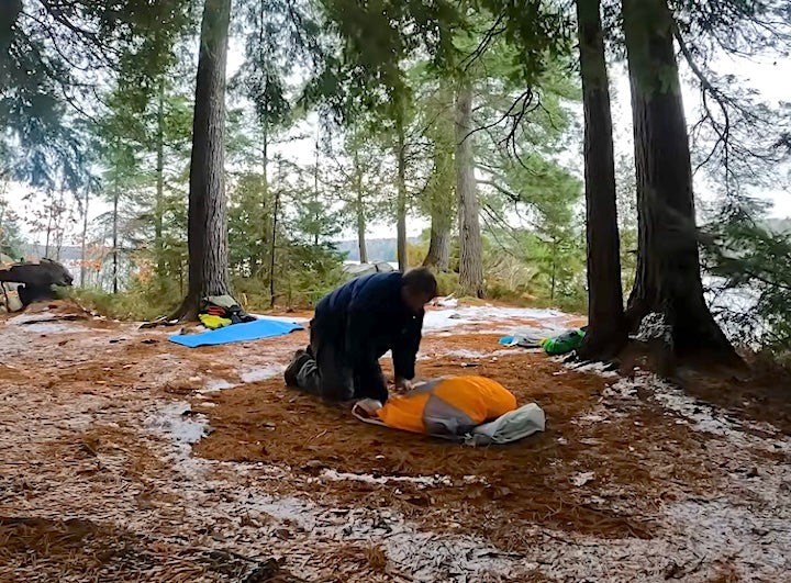 kayak camper rolls up his tent, ready to break a winter campsite