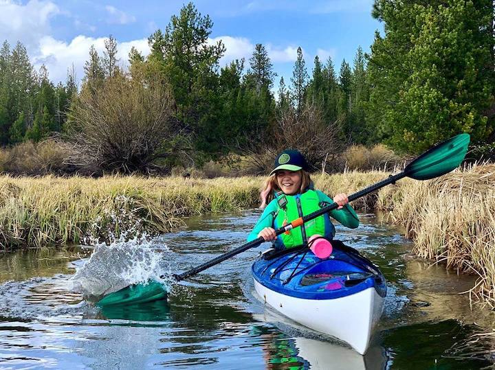 young girl kayaking in a blue kayak on a lake