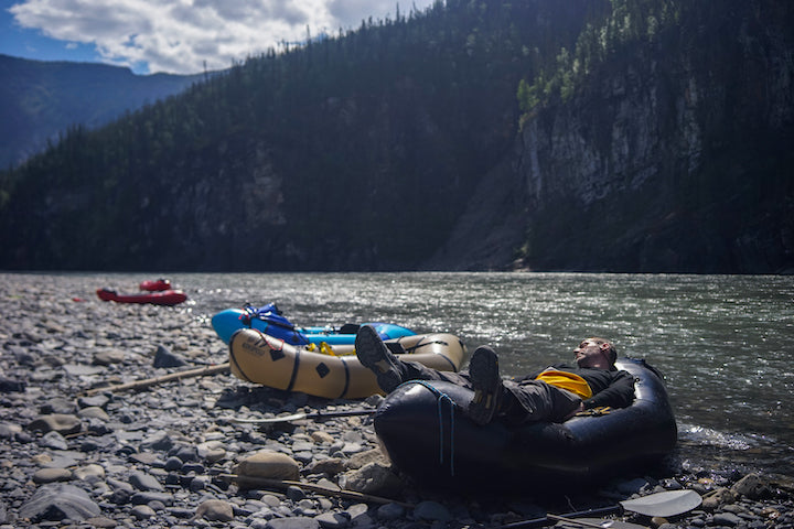 man naps on a packraft on shore, other packrafts next to him