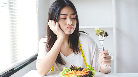 Frau schaut genervt auf ihre Gabel mit Salat