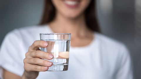 Falten vorbeugen: Frau hält ein Glas Wasser in der Hand