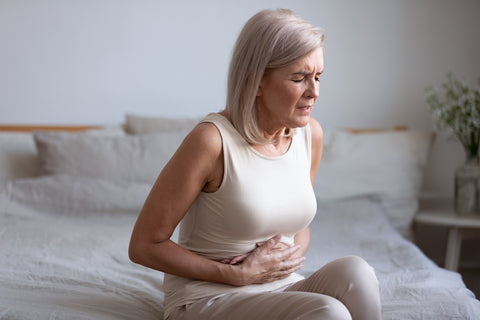 Frau sitzt auf dem Bett und hält sich den Bauch vor Schmerzen