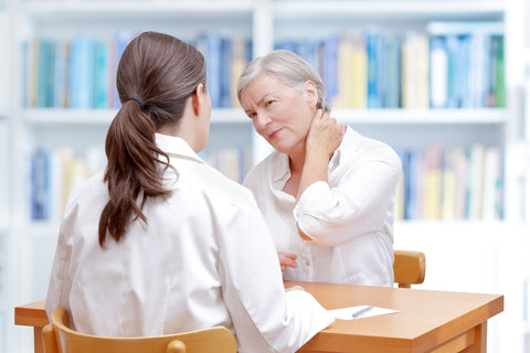 Frau mit Nackenschmerzen im Gespräch mit einer Ärztin