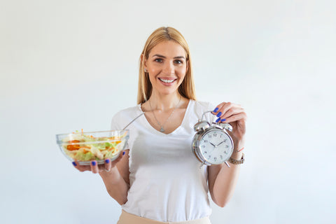 Frau hält Schüssel mit Salat und einen Wecker in den Händen