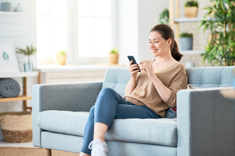 Frau sitzt auf Sofa und freut sich über Fotos auf dem Handy