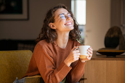Abnehmen mit Schilddrüsenunterfunktion: Frau sitzt glücklich mit Tasse Kaffee auf der Couch