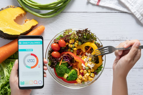 Kaloriendefizit berechnen: App zum Kalorientracken auf einem Smartphone und eine Schüssel mit Salat