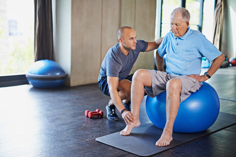 Mann macht mit einem Trainer Übungen auf einem Gymnastikball